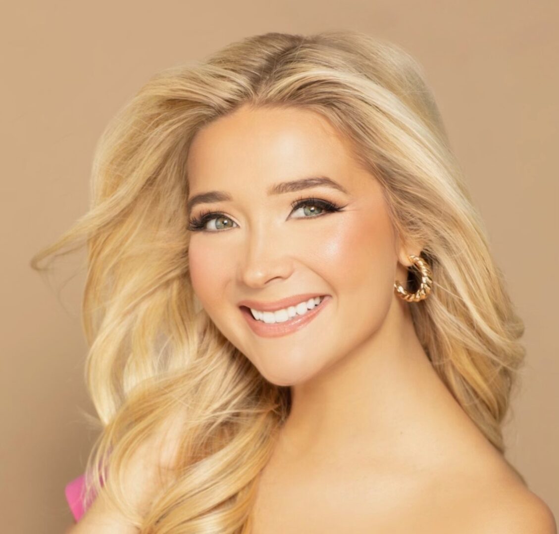 Woman with blonde hair smiling with gold earrings.