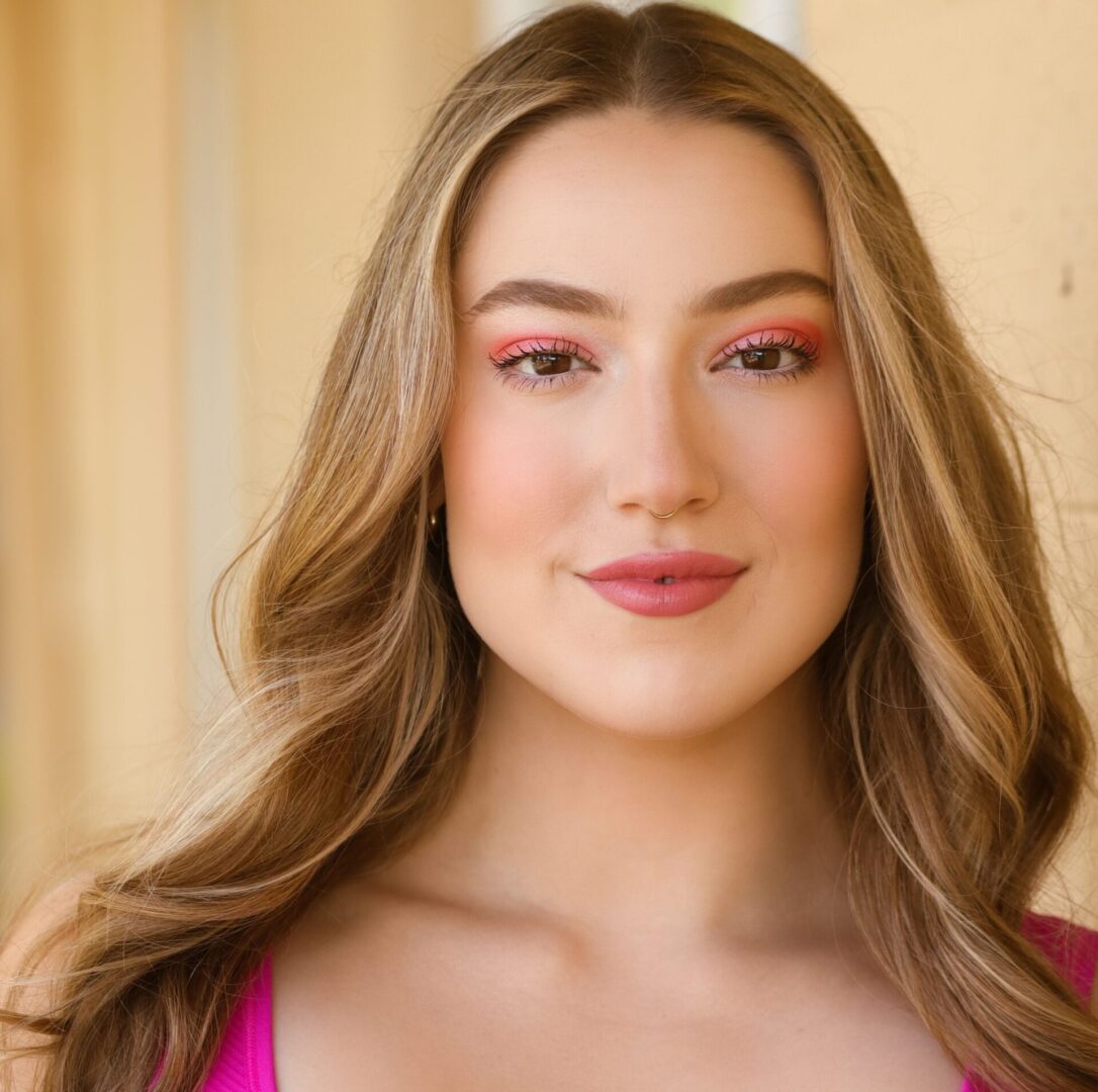 Smiling woman with long blonde hair and pink eyeshadow.