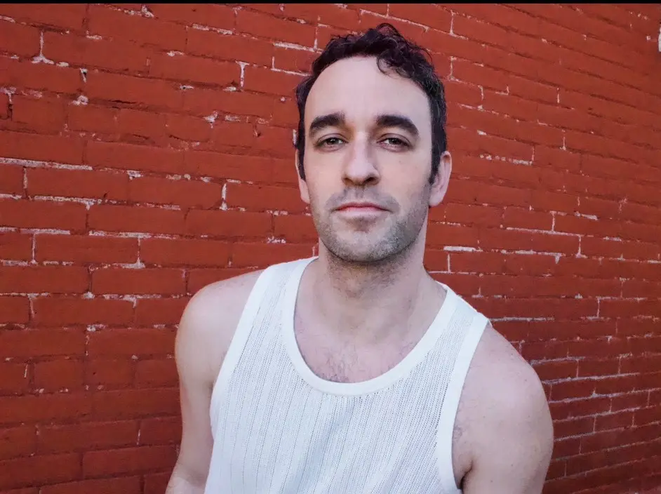 Man in a white tank top against a brick wall.