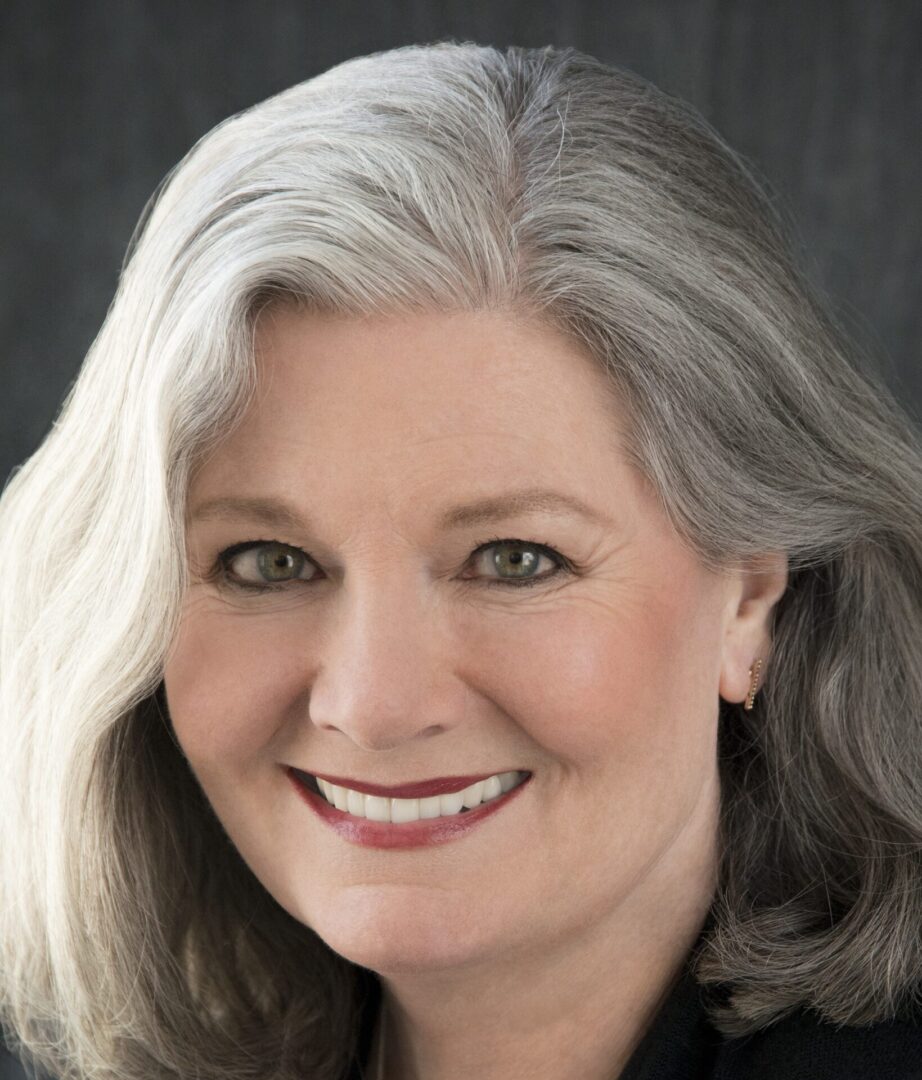 Smiling woman with gray hair and earrings.