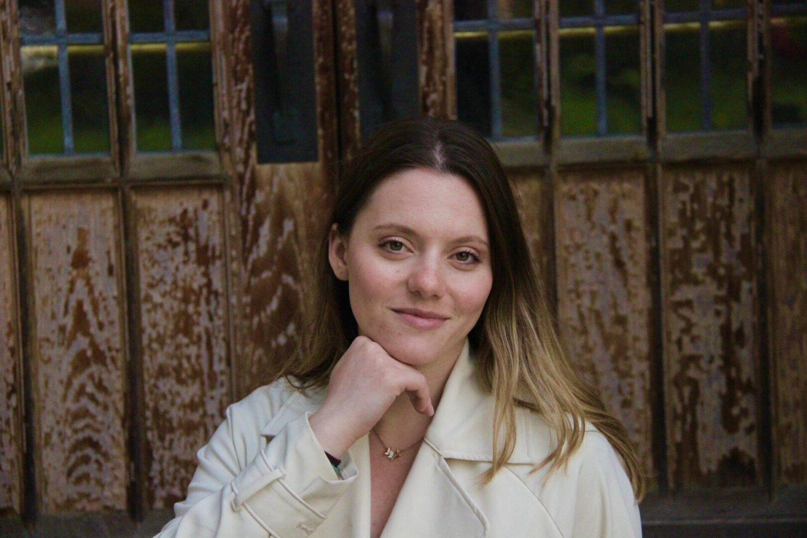 Smiling woman in white coat against wooden door.